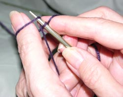 Notice the loop of yarn around the left thumb. With your right hand, insert the knitting needle through the underside of this loop