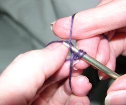 Moving the knitting needle toward you, draw the yarn through the loop of yarn on the left thumb